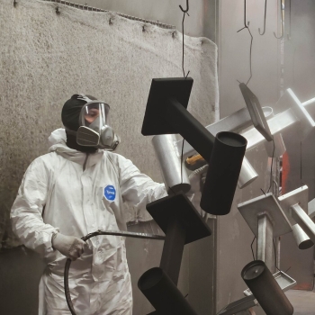 Technician applying industrial powder coating to metal parts in spray booth - Solera Brampton Ontario